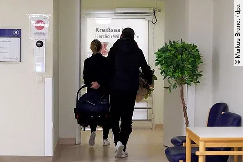 Paar mit Babyschale vor Kreißsaal: Seit der Schließung der Geburtsstation auf Sylt müssen Schwangere für die Entbindung aufs Festland – selbst Notfälle können nicht mehr vor Ort versorgt werden.
