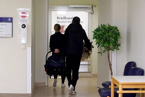 Paar mit Babyschale vor Kreißsaal: Seit der Schließung der Geburtsstation auf Sylt müssen Schwangere für die Entbindung aufs Festland – selbst Notfälle können nicht mehr vor Ort versorgt werden.