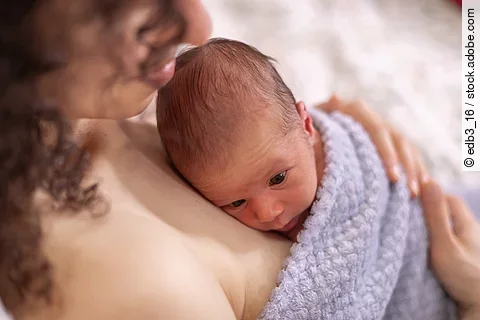 Adorable Newborn Baby Boy sitting on mother chest. Skin to Skin