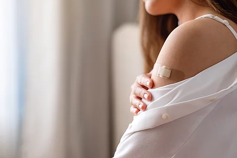 Closeup image of a young woman with adhesive bandage, medical plaster, band aid on her shoulder for vaccination concept
