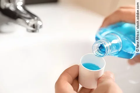 Man pouring mouthwash from bottle into cap in bathroom, closeup.