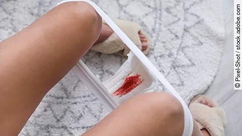 Young woman with dirty menstrual pad sitting on toilet bowl in bathroom, closeup