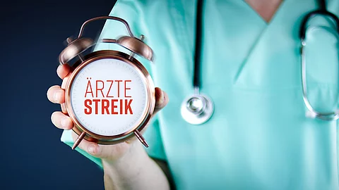 Ärztestreik. Arzt zeigt Wecker/Uhr mit Text. Hintergrund blau.