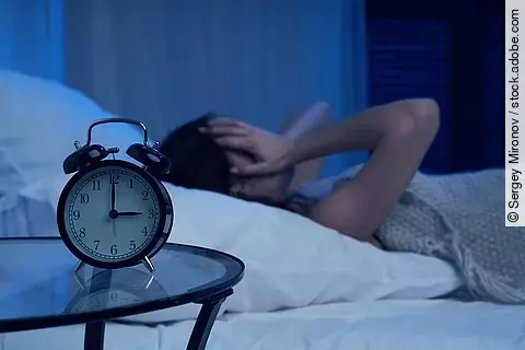 Unhappy woman with insomnia lying on bed next to alarm clock at night