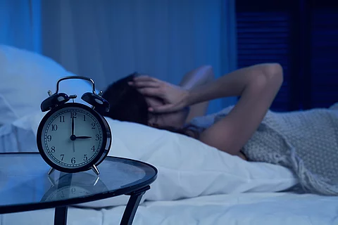 Unhappy woman with insomnia lying on bed next to alarm clock at night