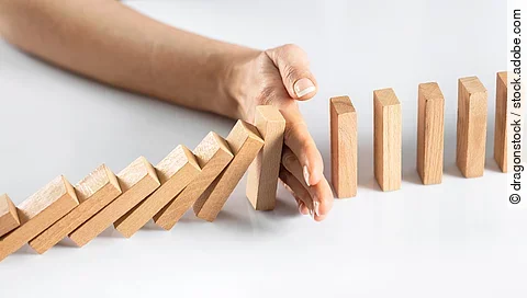 Dominosteine - eine Hand stoppt dem Dominoeffekt