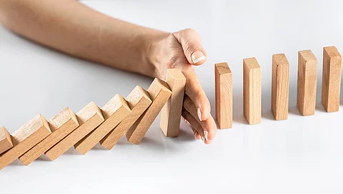 Dominosteine - eine Hand stoppt dem Dominoeffekt