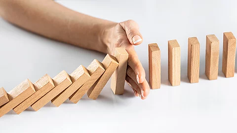 Dominosteine - eine Hand stoppt dem Dominoeffekt