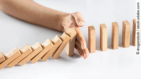 Dominosteine - eine Hand stoppt dem Dominoeffekt