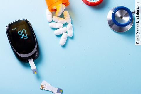 White pills in orange bottle with blood glucose meter on blue background with copy space