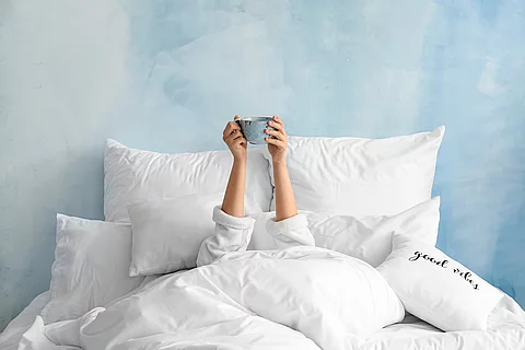 Young woman with cup of hot beverage lying in bed