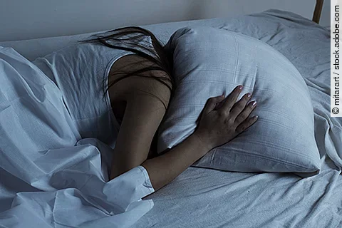 Frau in Bett hält sich Kissen über den Kopf
