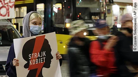 Vermummte Frau hält Protestschild hoch