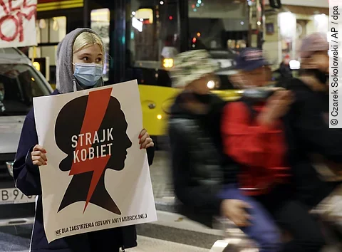 Vermummte Frau hält Protestschild hoch