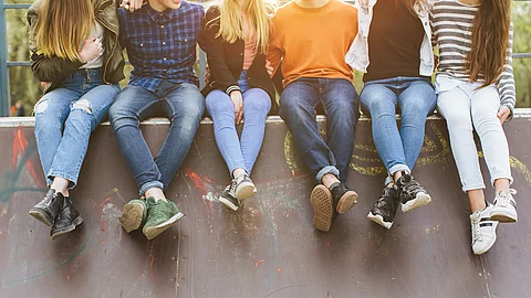 Sechs junge Menschen sitzen nebeneinander auf einer Mauer, ihre Beine baumeln herunter