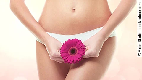Eine violette Gerbera vor dem weiblichen Intimbereich - Sinnbild für sexuelle Gesundheit