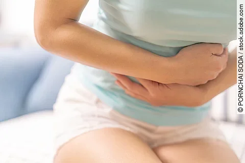 Young woman suffering from abdominal pain while sitting on the sofa and feeling stomachache, symptom of pms