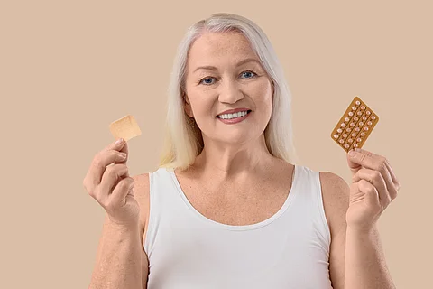 Mature woman with contraceptive patch and pills on beige background. Menopause concept