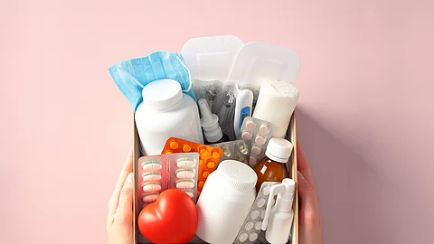 Box with essential healthcare kit with medication, pills, bandages, and face mask in female hands. Medical donations, first aid kit, home delivery of medications, online pharmacy concept. Arzneimittel in einer Box: Medikamente werden häufiger online gekauft